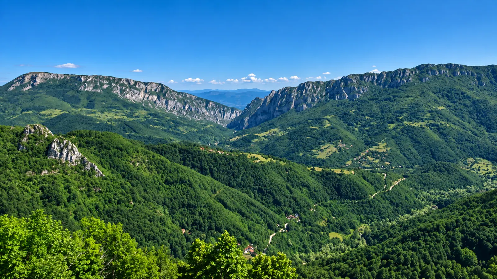 Zelena planinska dolina sa stenovitim grebenima pod vedrim nebom